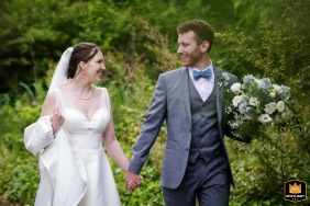 A bride and groom walk hand-in-hand at the London Wetland Centre. The photo captures them moving together, with the natural setting visible in the background.